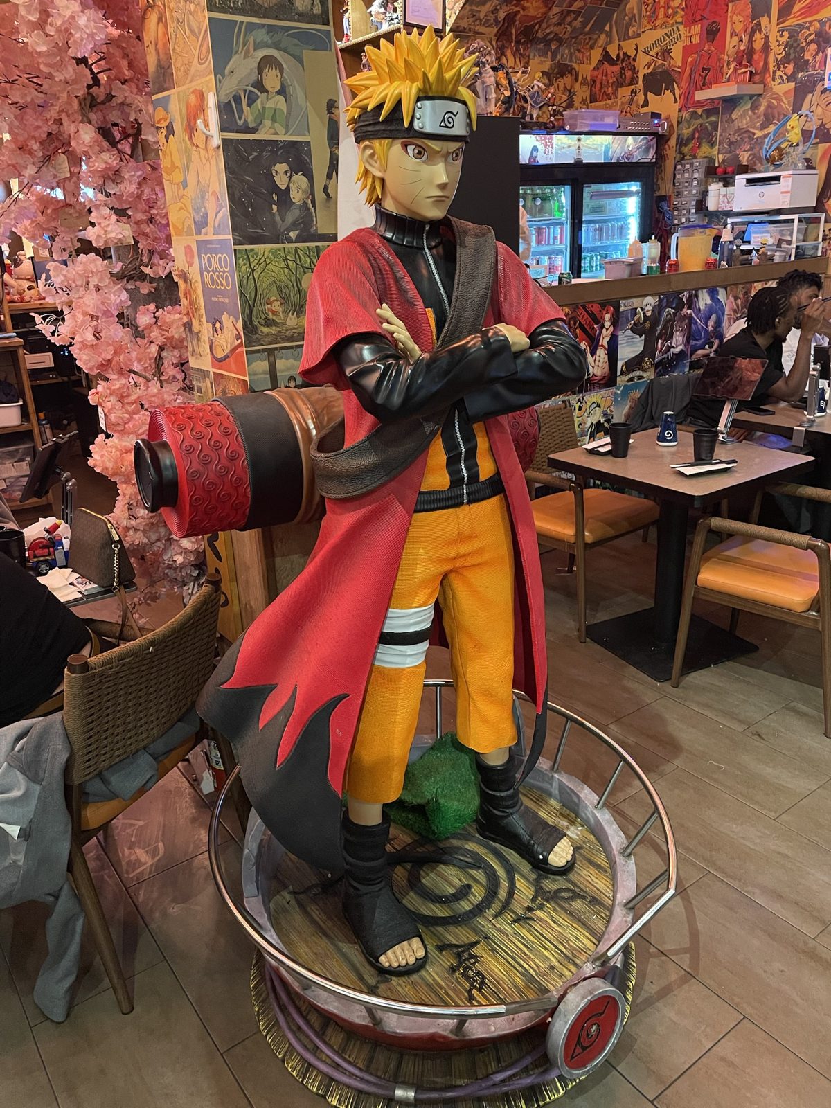 Statue grandeur nature de Naruto en mode ermite, bras croisés, sur un socle au symbole de Konoha